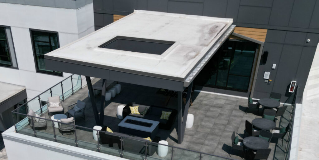 Modern rooftop outdoor lounge area with seating and glass railing, part of commercial building.