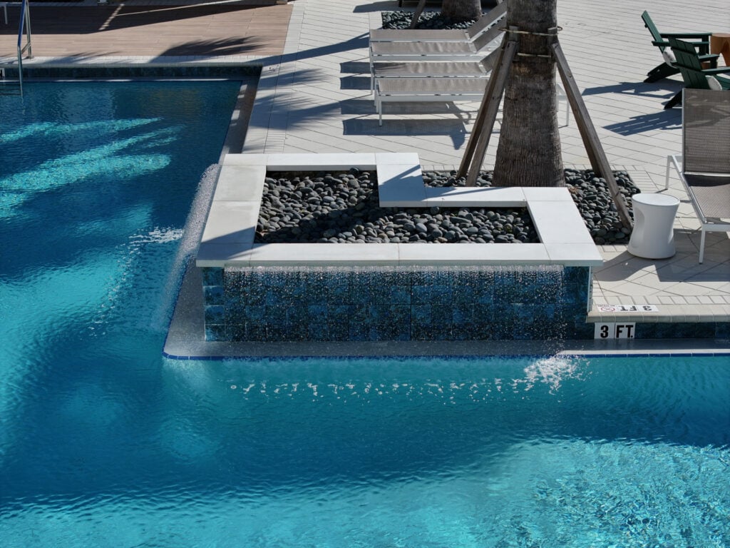 Modern swimming pool with decorative stone water feature and outdoor seating area.