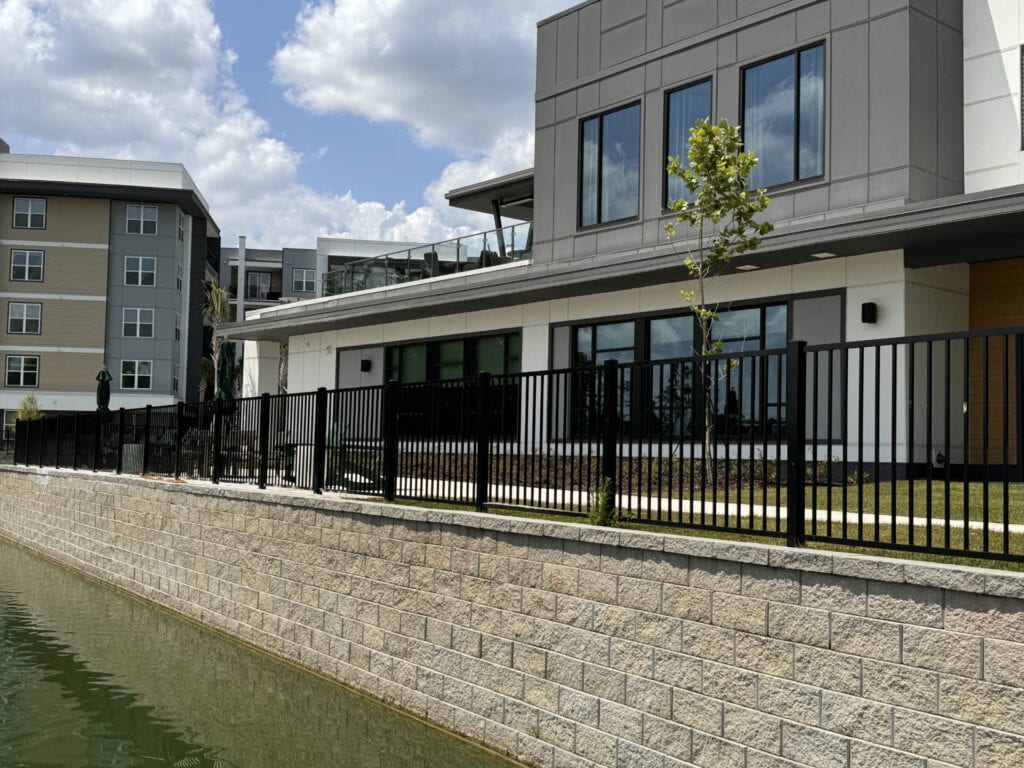 Modern residential building with outdoor patio and black metal fence near water.