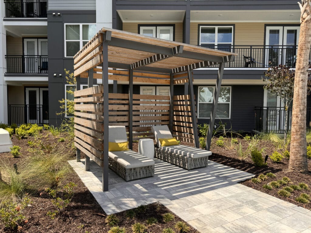 Modern outdoor sunshade with lounge chairs and landscaped garden in a residential complex.