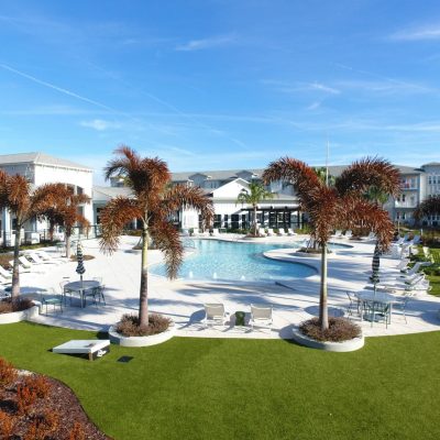 Luxury apartment pool area with palm trees and outdoor seating.