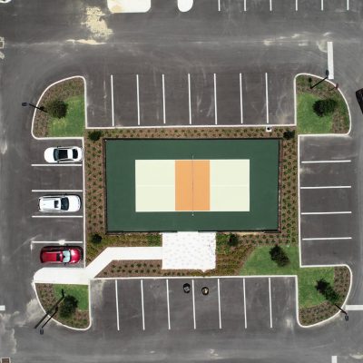 Sports court with parking lot and landscaped areas, aerial view of outdoor hardscapes.