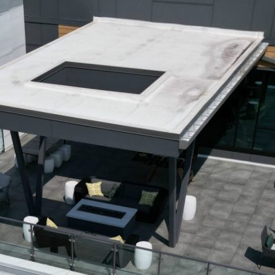 Modern rooftop outdoor lounge area with seating and glass railing, part of commercial building.
